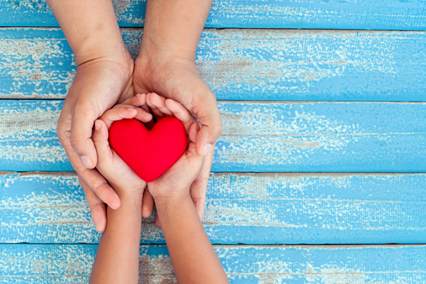 photo of a red heart laying in a small set of hands, those hands are laying in a bigger set of hands
