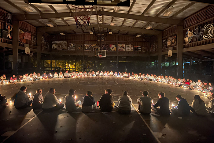 Photo of a group of teens sitting in a large circle in a gym in Israel holding candles