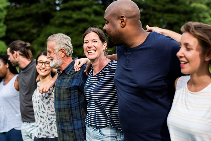 Photo of a group of people lined up with their arms around either other; they are smiling