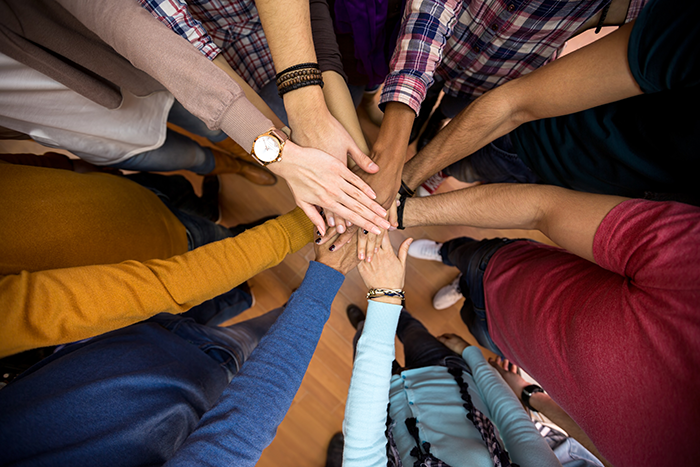 Photo of hands and arms in the middle of a team huddle, stacked on top of each other