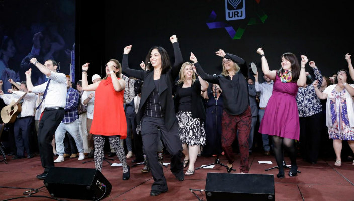 People dancing on stage at a past URJ Biennial with the URJ logo visible in the background