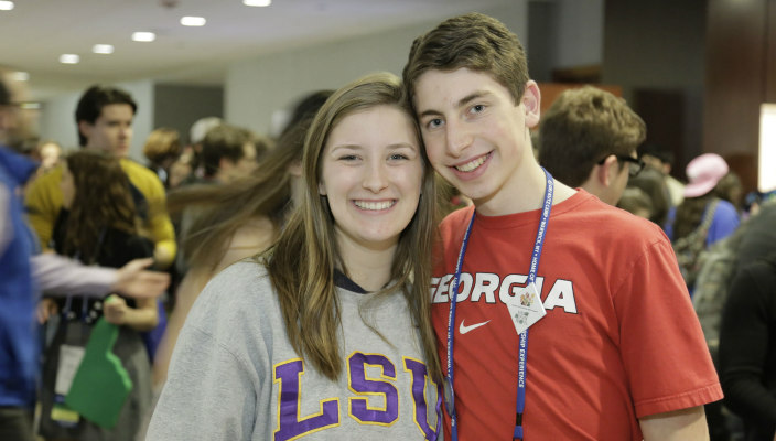 Male and female graduating NFTY seniors with their arms around one another while wearing college tee shirts 