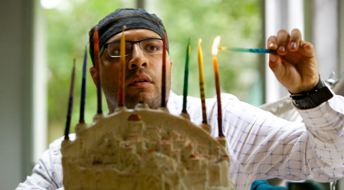 Young man kindling candles in a hanukkiyah