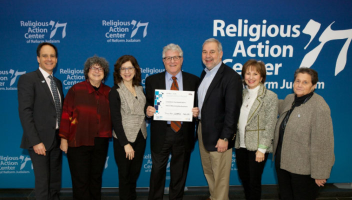 Past Fain Award winners posing in front of a Religious Action Center banner with their award