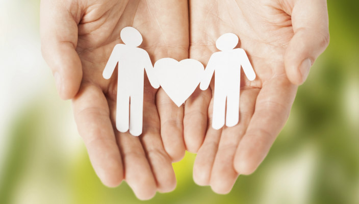 Cupped hands holding a paper cutout of two male shaped stick figures with a heart between them