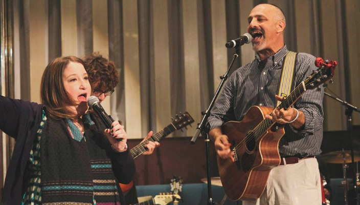 Man and woman playing guitars and singing while leading worship services