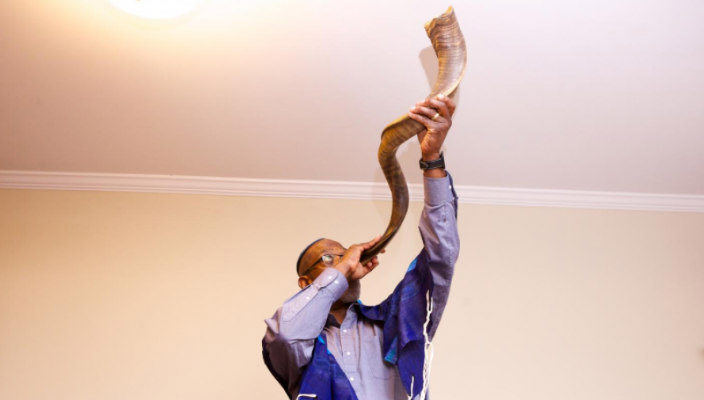 Man blowing a shofar high into the air in front of a white background