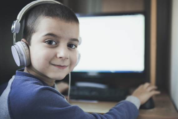 Boy wearing headphones and looking over his shoulder from a desk with a computer