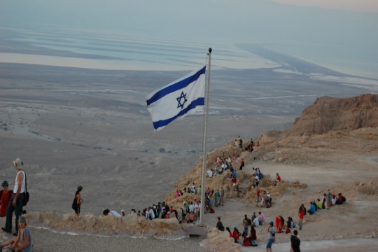 Israeli flag on flagpole in desert, populated by visitors