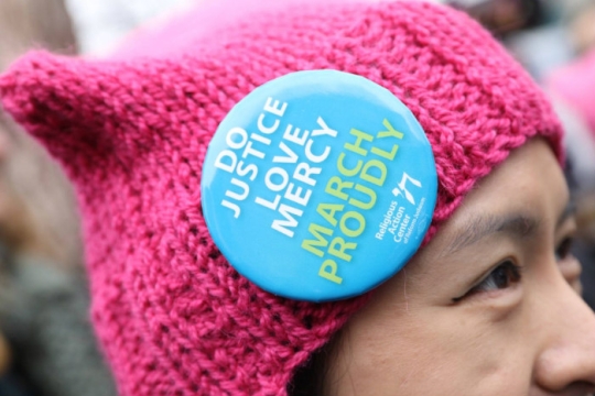 woman at protest march wearing hat with pin that says Do Justice Love Mercy March Proudly