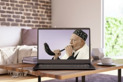 Laptop on a table in a living room displaying a man in a kippah blowing a shofar