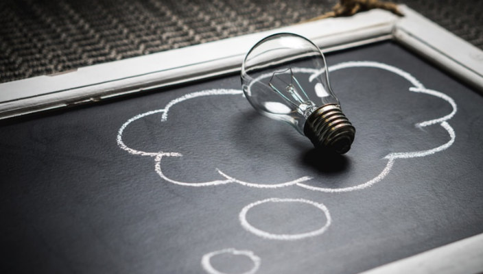 Light bulb sitting atop a thought bubble drawn in chalk on a chalkboard